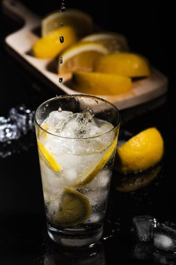 Köpüklü soğuk su Detoks limon dilimleri ve buz siyah arka bir karanlık cam zemin üzerine dökülen