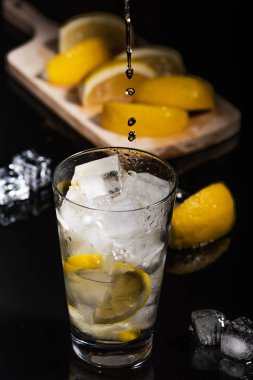 Köpüklü soğuk su Detoks limon dilimleri ve buz siyah arka bir karanlık cam zemin üzerine dökülen