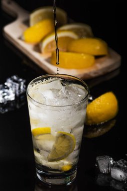 Köpüklü soğuk su Detoks limon dilimleri ve buz siyah arka bir karanlık cam zemin üzerine dökülen