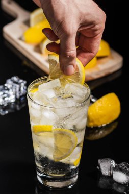 Ayrıntılar için lezzetli cin tonik karışık içmek kokteyl limon dilimleri ile bitirmek ve buz küpleri, siyah arka plan üzerine barmen eller