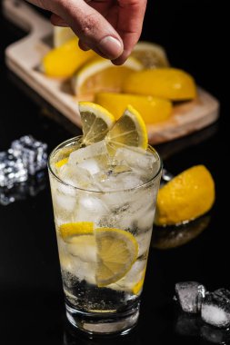 Ayrıntılar için lezzetli cin tonik karışık içmek kokteyl limon dilimleri ile bitirmek ve buz küpleri, siyah arka plan üzerine barmen eller