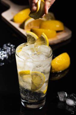 Ayrıntılar için lezzetli cin tonik karışık içmek kokteyl limon dilimleri ile bitirmek ve buz küpleri, siyah arka plan üzerine barmen eller