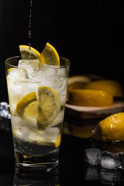 Maden suyu ya da limon dilimleri ile şeffaf diğer içki dökme ve buz küpleri güzel cam siyah arka plan yatay görünümünde