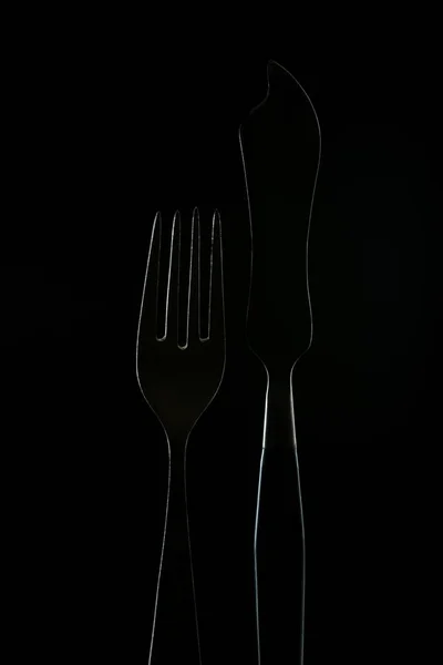 Fourchette et couteau à poisson, silhouette sombre, silhouette avec lumière, projecteur sur les sites, concept alimentaire, couteau avec chiffoline noir et fourchette en acier — Photo