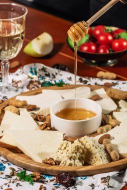 Peynir tabağı ve Şef el wich dökülen tatlım: Sulguni, bölgesinin, çedar, gouda, camembert ve diğer beyaz şarap ile hizmet bal ve fındık üzerinde ahşap tahta üzerinde ışık arka plan. Lezzetli mezeler.