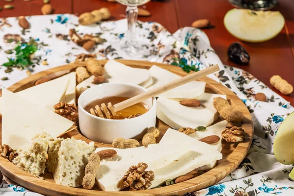 Ассорти сыров на круглой деревянной доске подается с белым вином Гуда сыр, тертый сыр кора дуба, твердые кусочки сыра, грецкие орехи, виноград, крекеры, мед, сульгуни, легкий деревянный фон — стоковое фото