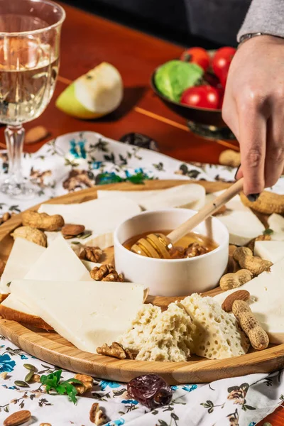 Assorted cheeses on round wooden board plate served with white wine Guda cheese, cheese grated bark of oak, hard cheese slices, walnuts, grapes, crackers, honey, sulguni, light wood background — Stock Photo, Image