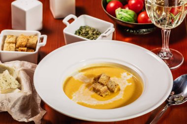 Kavrulmuş kabak ve havuç çorbası Krem, balkabağı tohumları ile. Kruton, peynir ve ahşap arka plan üzerinde beyaz şarap ile devam eder. Kopya alanı