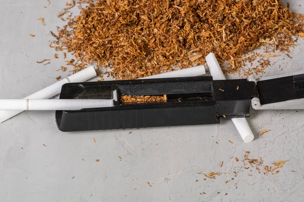 Cut and dried tobacco leaves. A device for making cigarettes at home. Homemade Tobacco Cigarette, copy paste space, in the gray background