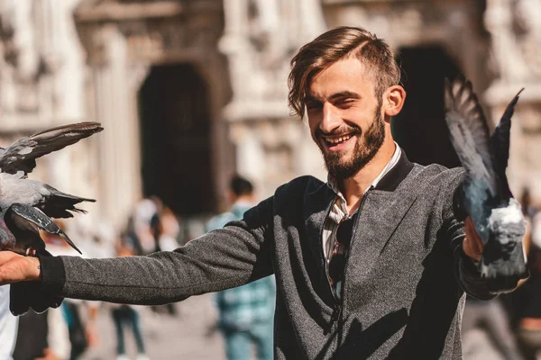 Happy Young man posing with pigeons in the milanese street with ancient church Duomo di Milano on background. Cute happy 23 years old man posing in Milan, Italy.