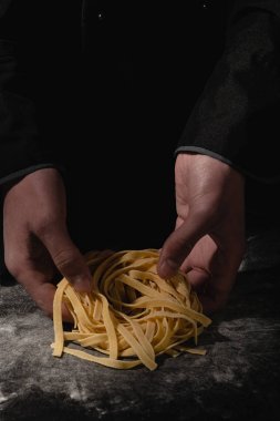 Şef eller ile siyah masada taze makarna ile spagetti, makarna, erişte yapma.
