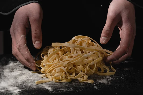 Chef hands making spaghetti, pasta, noodles with fresh pasta on black table with. — Stock Photo, Image
