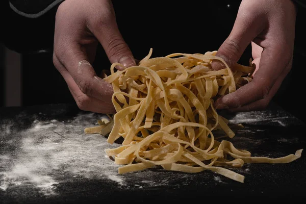 Chef hands making spaghetti, pasta, noodles with fresh pasta on black table with. — Stock Photo, Image