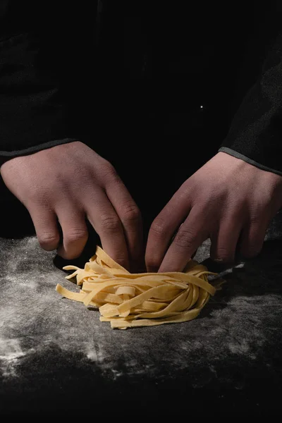 Chef hands making spaghetti, pasta, noodles with fresh pasta on black table with. — Stock Photo, Image