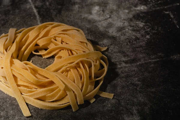 Isolated raw pasta on a black background with a place for text. Traditional Italian pasta, noodles, tagliatelle. Top view. Copy space. — Stock Photo, Image