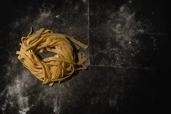 Isolated raw pasta on a black background with a place for text. Traditional Italian pasta, noodles, tagliatelle. Top view. Copy space. — Stock Photo, Image