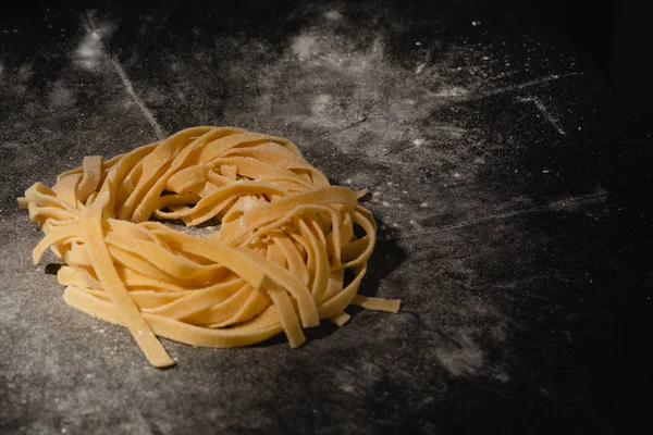 Isolated raw pasta on a black background with a place for text. Traditional Italian pasta, noodles, tagliatelle. Top view. Copy space. — Stock Photo, Image