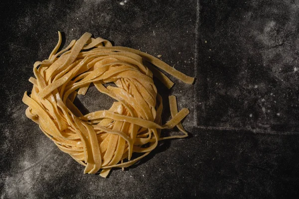 Isolated raw pasta on a black background with a place for text. Traditional Italian pasta, noodles, tagliatelle. Top view. Copy space.