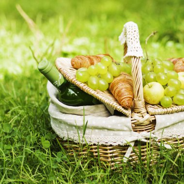 Yeşil üzüm, elma, bir şişe şarap ve yeşil çimenlerin üzerinde duran kruvasan ile Vintage hasır sepet