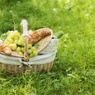 Vintage hasır sepet piknik yeşil üzüm ve şarap ile yeşil çimenlerin üzerinde duran kruvasan ile için