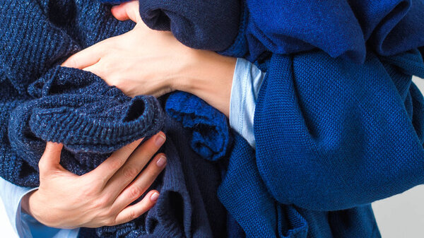 Close view of woman holding heap of blue woolen and cashmere sweaters on white background 