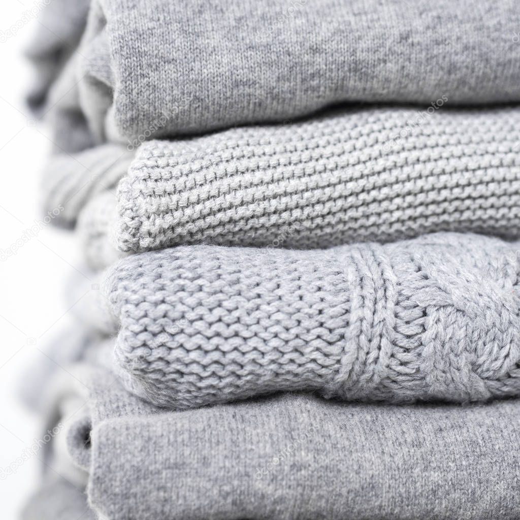 careful stack of grey woolen and cashmere sweaters on white background