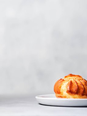 Muhallebi ile Fransız profiterol serpilir ve pudra şekeri gri arka plan üzerinde beyaz plaka üzerinde