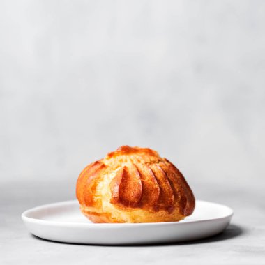 Muhallebi ile Fransız profiterol serpilir ve pudra şekeri gri arka plan üzerinde beyaz plaka üzerinde