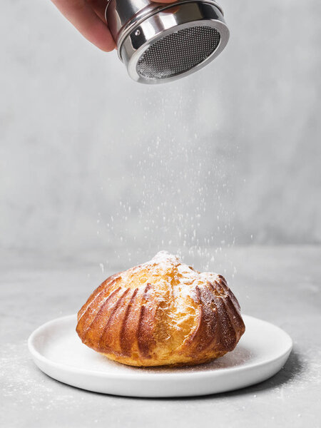 French profiterole with custard sprinkled and powdered sugar on white plate on gray background