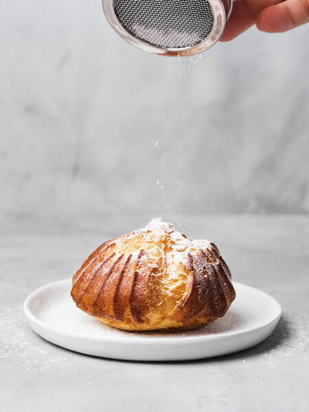 French profiterole with custard sprinkled and powdered sugar on white plate on gray background