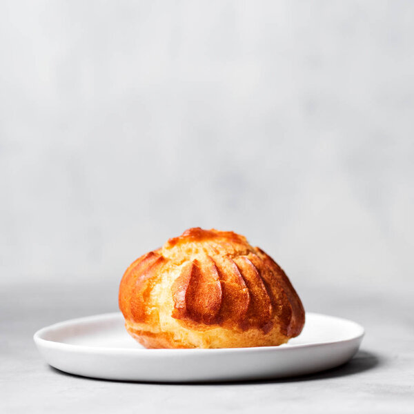 French profiterole with custard sprinkled and powdered sugar on white plate on gray background