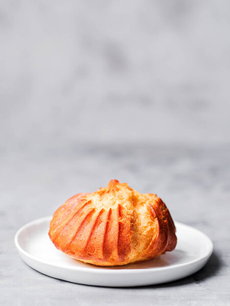 French profiterole with custard sprinkled and powdered sugar on white plate on gray background
