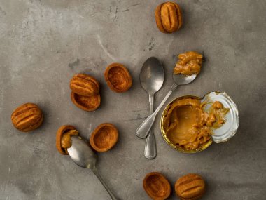 Vintage gümüş kaşıklarla karamelize süt ve gri beton zemin üzerine ceviz şeklinin kahverengi kurabiye