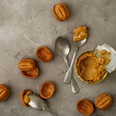 Vintage gümüş kaşıklarla karamelize süt ve gri beton zemin üzerine ceviz şeklinin kahverengi kurabiye