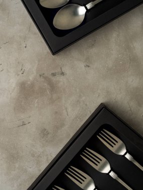 Gri beton zemin üzerine Çatallarla kaşıklar siyah kutular içinde gümüş koleksiyonunun üstten görünüm