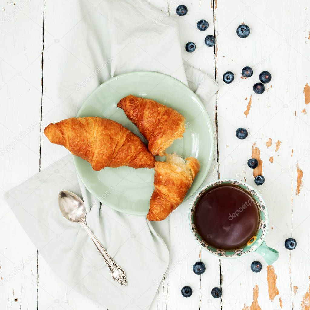 Top view of fresh croissants served with ripe blueberries and cup of tea 
