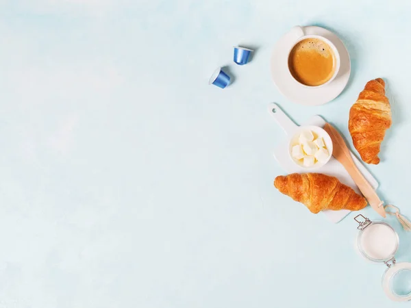 Cup of coffee with capsules, croissants and butter on blue pastel background
