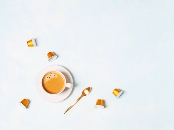 cup of coffee espresso with capsules and golden spoon on blue pastel background