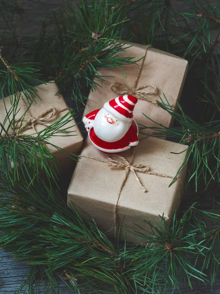 Close view of Christmas gifts in kraft paper with ceramic vintage Santa Claus toy in fir branches