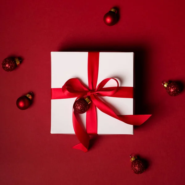 礼物白色盒子的顶部视图与红色丝带装饰与红色闪光球在红色背景 — 图库照片