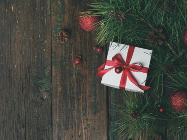 Beyaz hediye kutusu kırmızı kurdele ve glitter topları Çamın dalları ve koyu ahşap arka plan, yakın çekim, Noel ve Yılbaşı Konsept koniler ile dekore edilmiştir 
