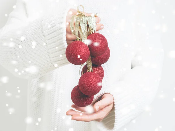 Woman in warm white sweater holding pile of red Christmas baubles with snowfall effect , Concept for New year mock-up