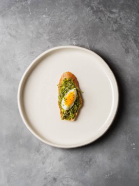 Tam tahıllı ekmek en iyi görünümü yumurta, taze mini otlar ve gri beton zemin üzerine serpilir siyah tuz ile avokado kaplama