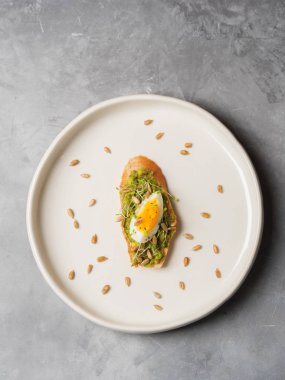 tam tahıllı ekmek, yumurta, taze mini otlar, ayçekirdeği ve beyaz tabakta serpilir siyah tuz ile avokado kaplama