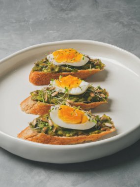 Üç tam tahıllı görünümü Kapat yumurta, taze mini otlar, ayçekirdeği ve beyaz seramik tabakta serpilir siyah tuz ile kaplama avokado kızartır