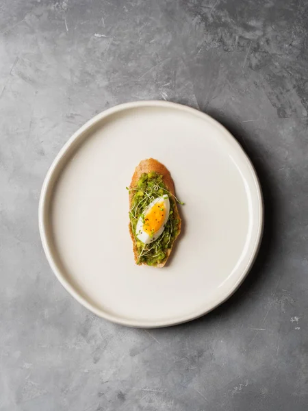 Tam tahıllı ekmek en iyi görünümü yumurta, taze mini otlar ve gri beton zemin üzerine serpilir siyah tuz ile avokado kaplama