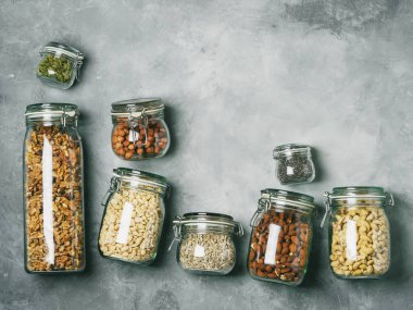 Yığın cam kavanozlar badem, kaju fıstığı, fıstık, fındık, ceviz ve Chia Tohumu, beton zemin üzerine ayçiçeği ve kabak çekirdeği ile