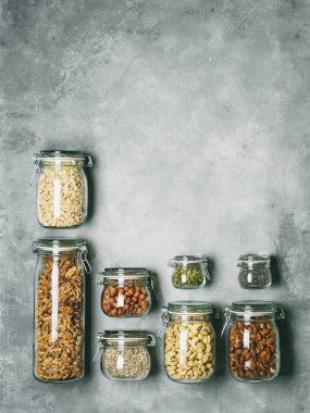 Yığın cam kavanozlar badem, kaju fıstığı, fıstık, fındık, ceviz ve Chia Tohumu, beton zemin üzerine ayçiçeği ve kabak çekirdeği ile