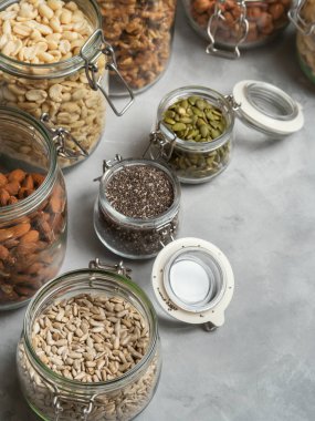 Badem, kaju fıstığı, fıstık, fındık, ceviz ve Chia tohum çeşitliliği, beton zemin üzerine ayçiçeği ve kabak çekirdeği cam kavanozlar