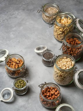 Badem, kaju fıstığı, fıstık, fındık, ceviz ve Chia tohum çeşitliliği, beton zemin üzerine ayçiçeği ve kabak çekirdeği cam kavanozlar